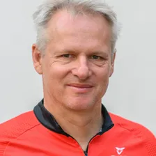 Portraitfoto von lächelndem Mann mit rotem Trikot vor grauem Hintergrund
